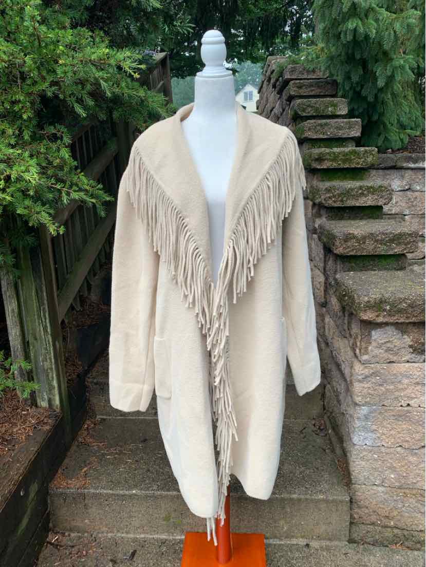 Tan oversized coat with wide fringe trim along collar and front edges, long sleeves.