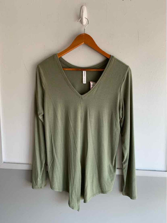 Olive green long-sleeve V-neck top hanging on wooden hanger against white wall.
