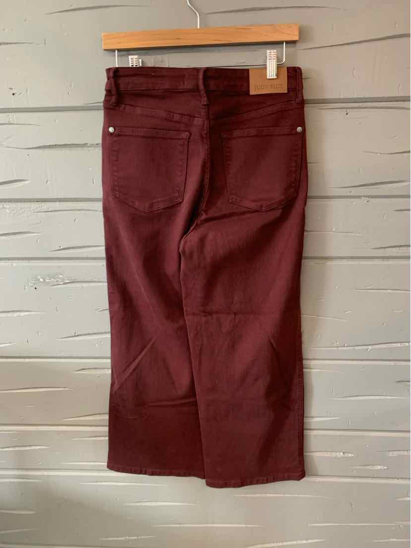 Burgundy denim jeans with back pockets and contrast stitching, hanging on wooden hanger.