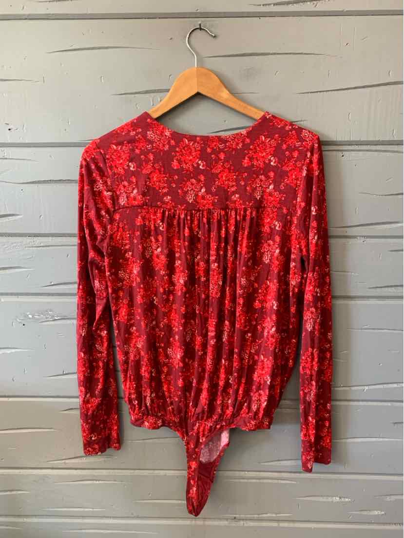 Red floral long-sleeve blouse with a gathered waist and pointed front hem, hanging on a wooden hanger.