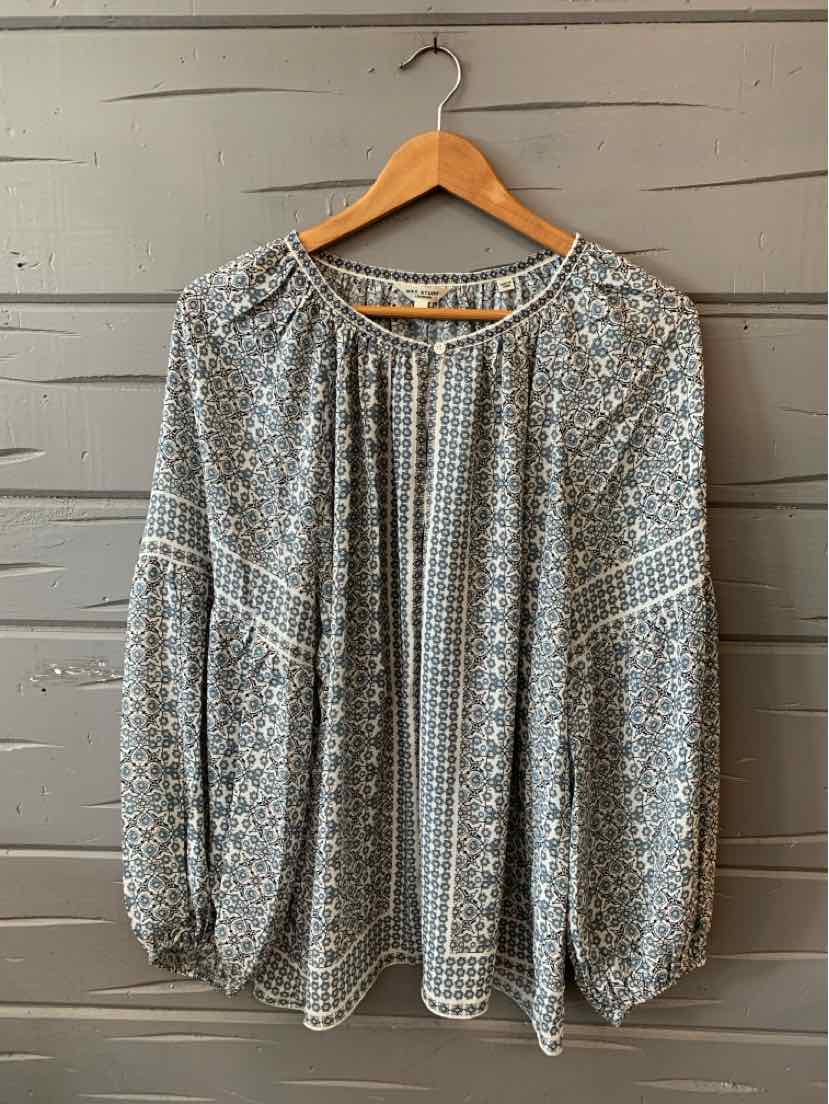 Light blue patterned long-sleeve blouse with gathered neckline and loose fit on wooden hanger.