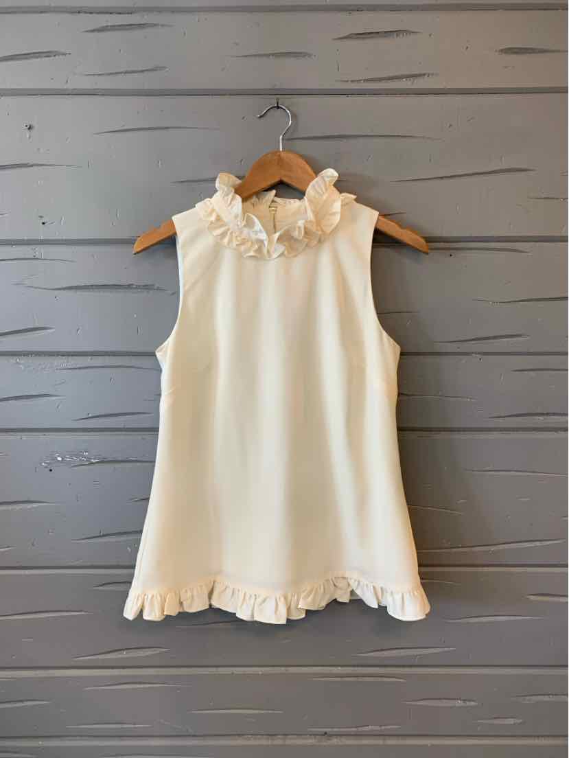 Cream sleeveless blouse with ruffled collar and hem on wooden hanger against gray wooden wall.