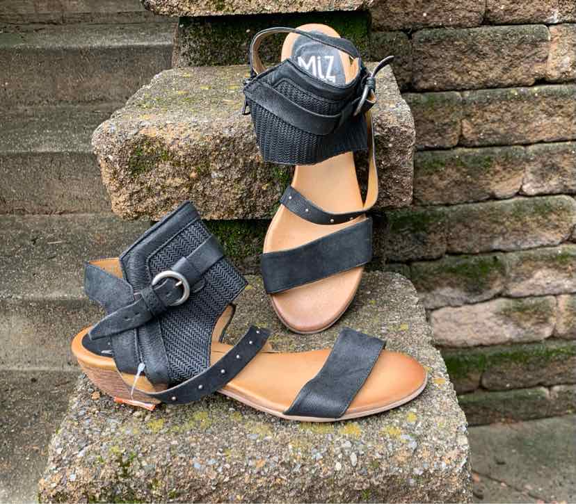 Black leather sandal with ankle strap, buckle closure, and low wooden wedge heel.
