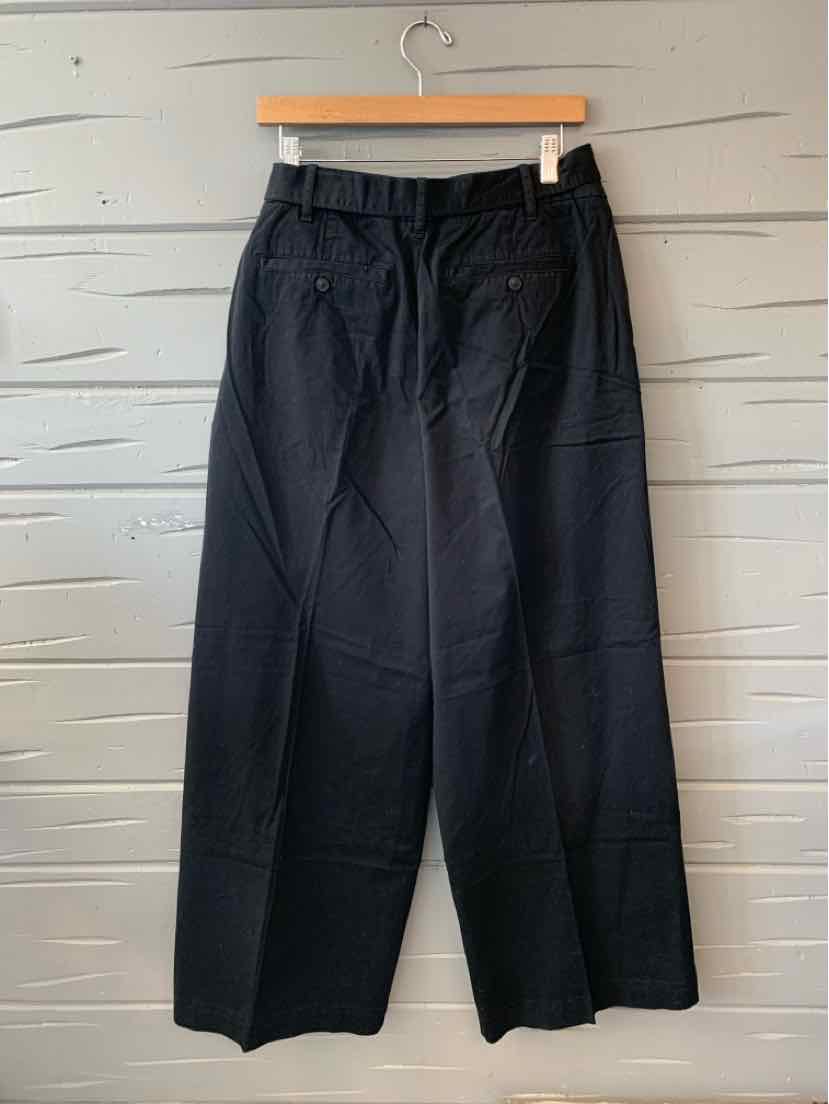 Black high-waist wide-leg pants with front pockets and belt loops hanging on wooden hanger against gray wall.