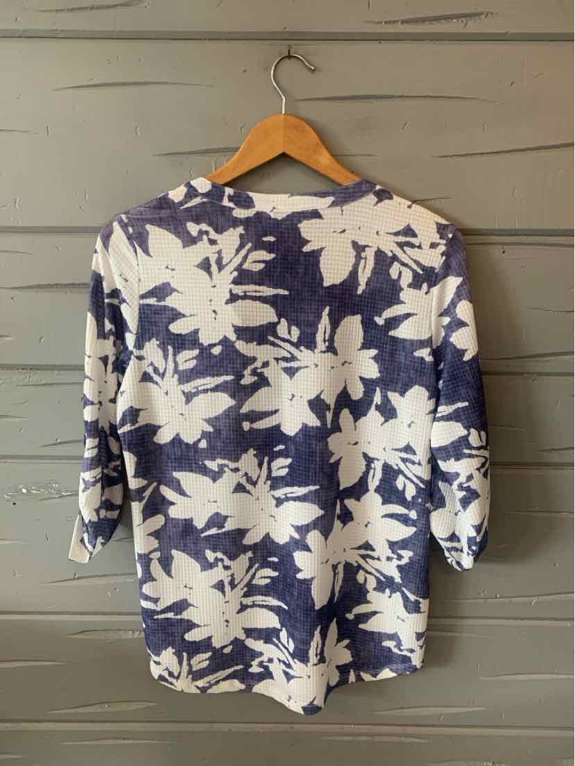 Woman’s navy blue top with large white floral print and three-quarter sleeves hanging on wooden hanger.