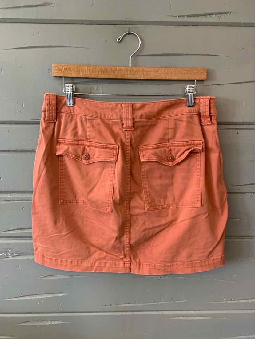 Rust-orange casual mini skirt with front pockets and a button closure waistband.