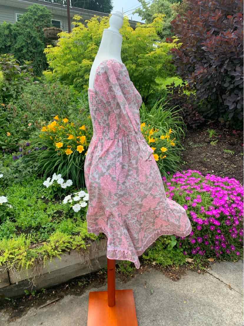 Pink floral sleeveless dress with fitted bodice and flared skirt on wooden mannequin outdoors.