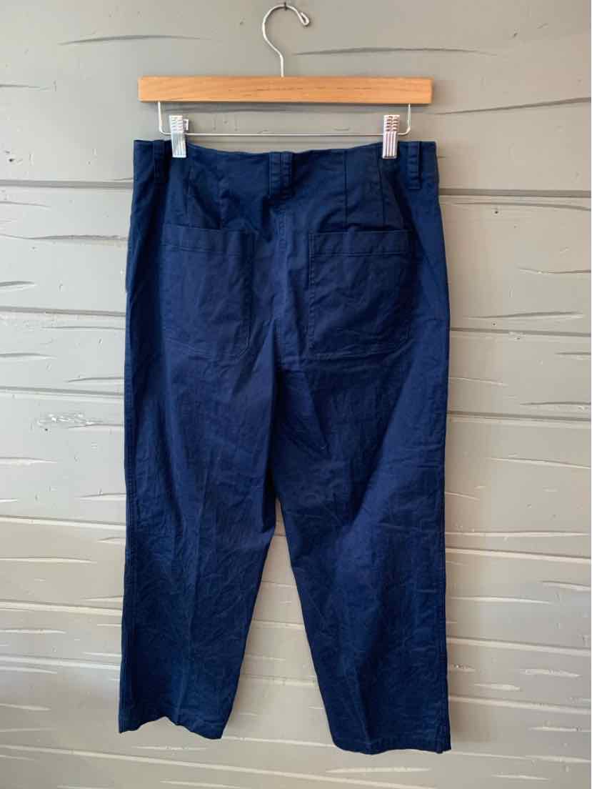 Navy blue straight-leg pants with a high waist and back patch pocket, hanging on wooden hanger against gray wooden wall.