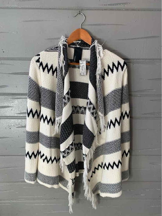 Black and white patterned open-front cardigan with zigzag and stripe designs on wooden hanger.