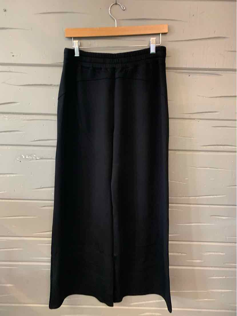 Black wide-leg pants with elastic waistband, smooth solid fabric, hanging on wooden hanger.