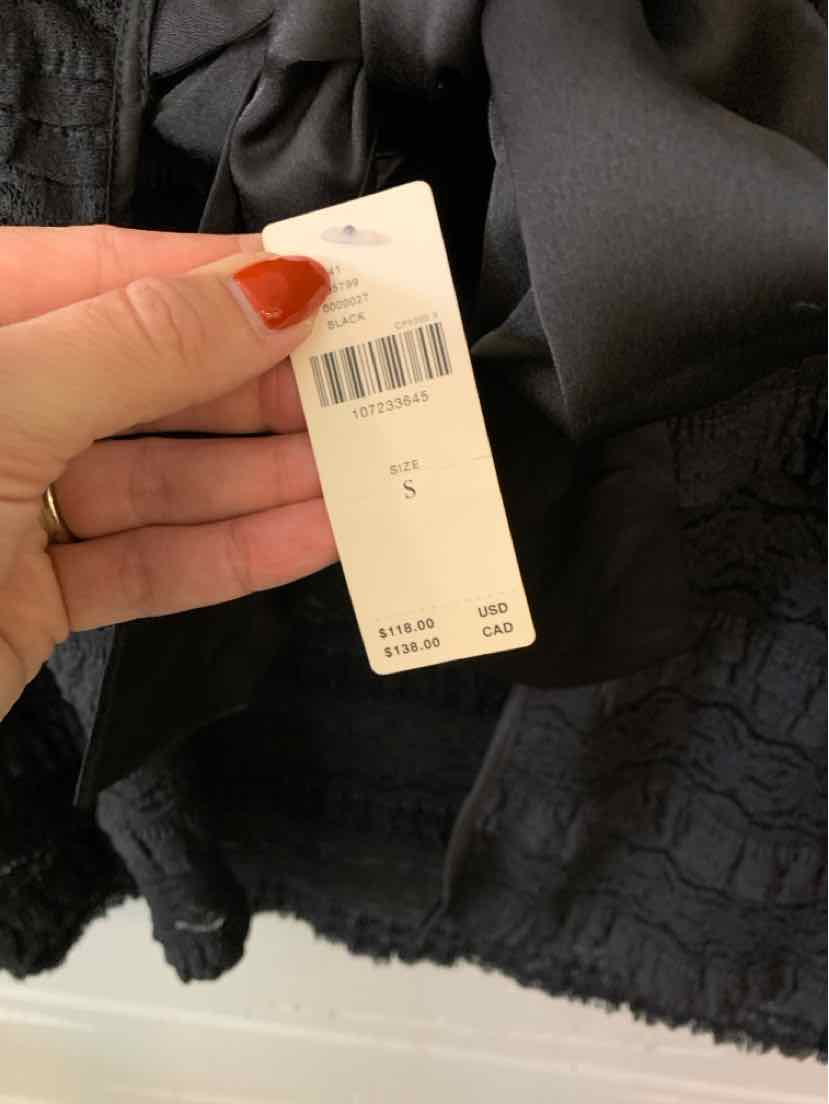 Black lace Lyrebird garment with a textured floral pattern and scalloped edge, shown with a white size tag.
