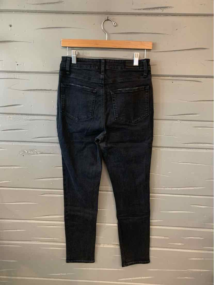 Black high-waist skinny jeans with back pockets hanging on wooden hanger against beige wall.