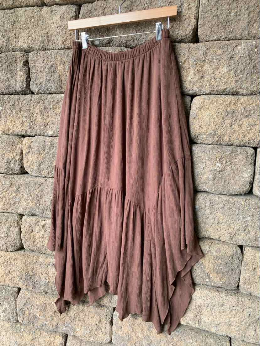 Flowy brown midi skirt with layered, asymmetrical hem and elastic waistband hanging on wooden hanger.