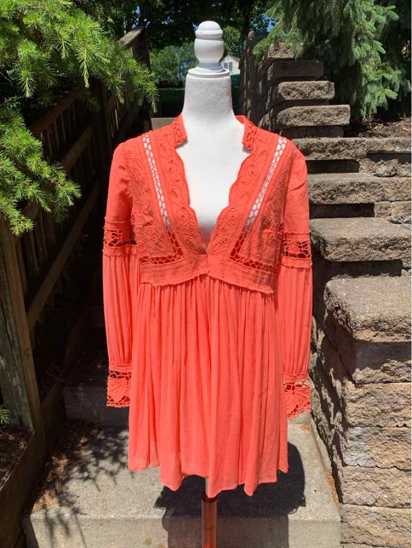 Coral long-sleeve mini dress with lace detailing and pleated skirt on mannequin.