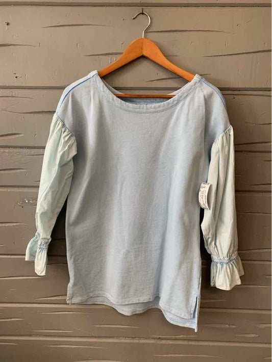 Light blue long-sleeve blouse with gathered ruffle cuffs and a boat neckline on wooden hanger.