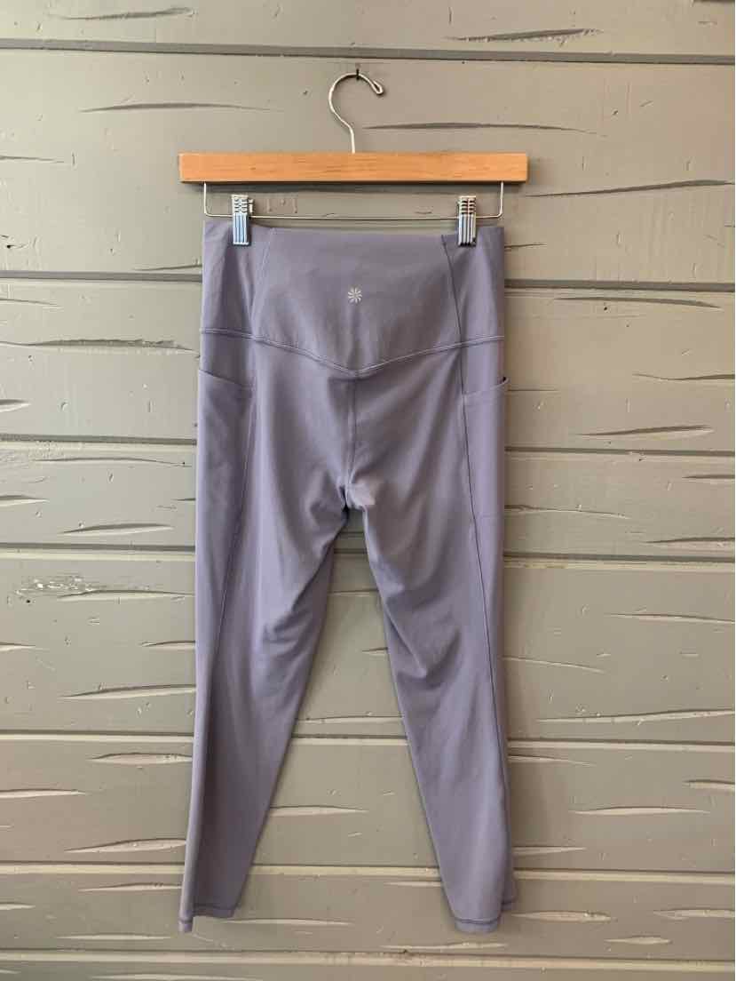 Mauve high-waist athletic leggings with flat seams hanging on a wooden hanger against a textured beige wall.