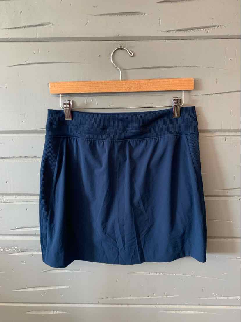 Navy blue athletic skirt with wide waistband and slight flare, hanging on wooden hanger against gray wooden wall.