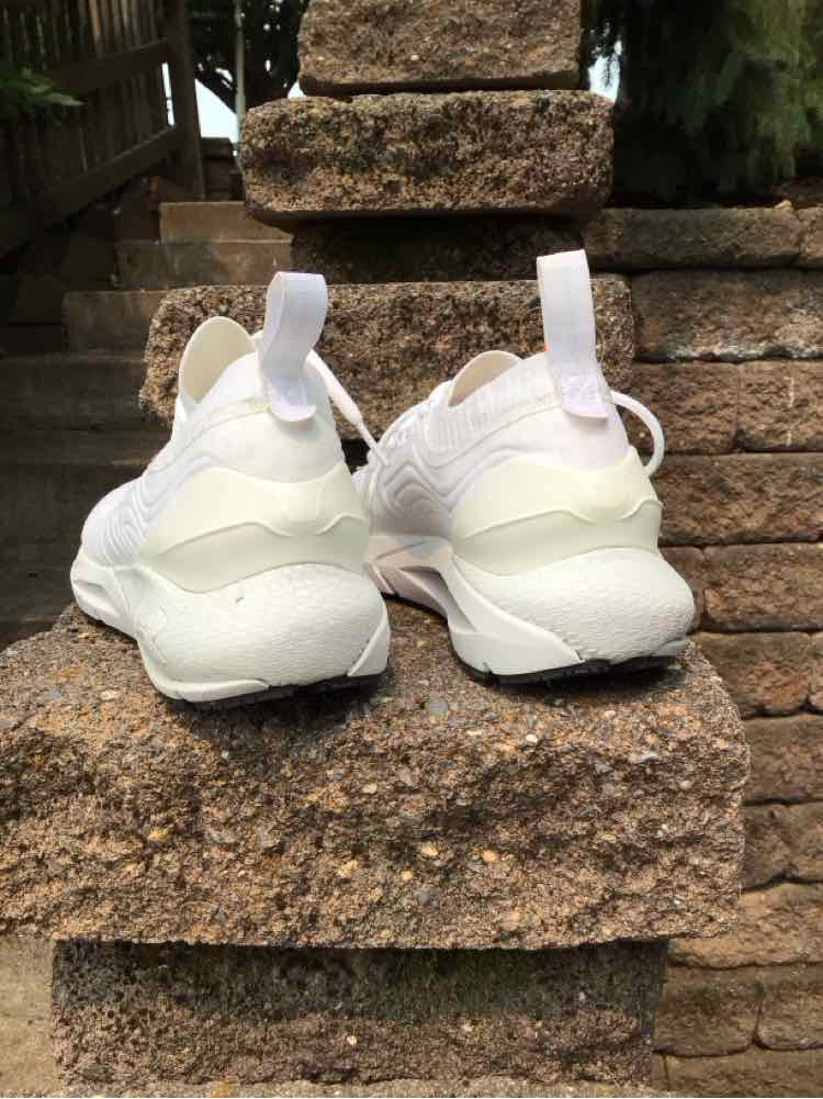 White Under Armour women's sneaker size 9.5 with mesh upper and pull tab heel, viewed from back on stone steps.