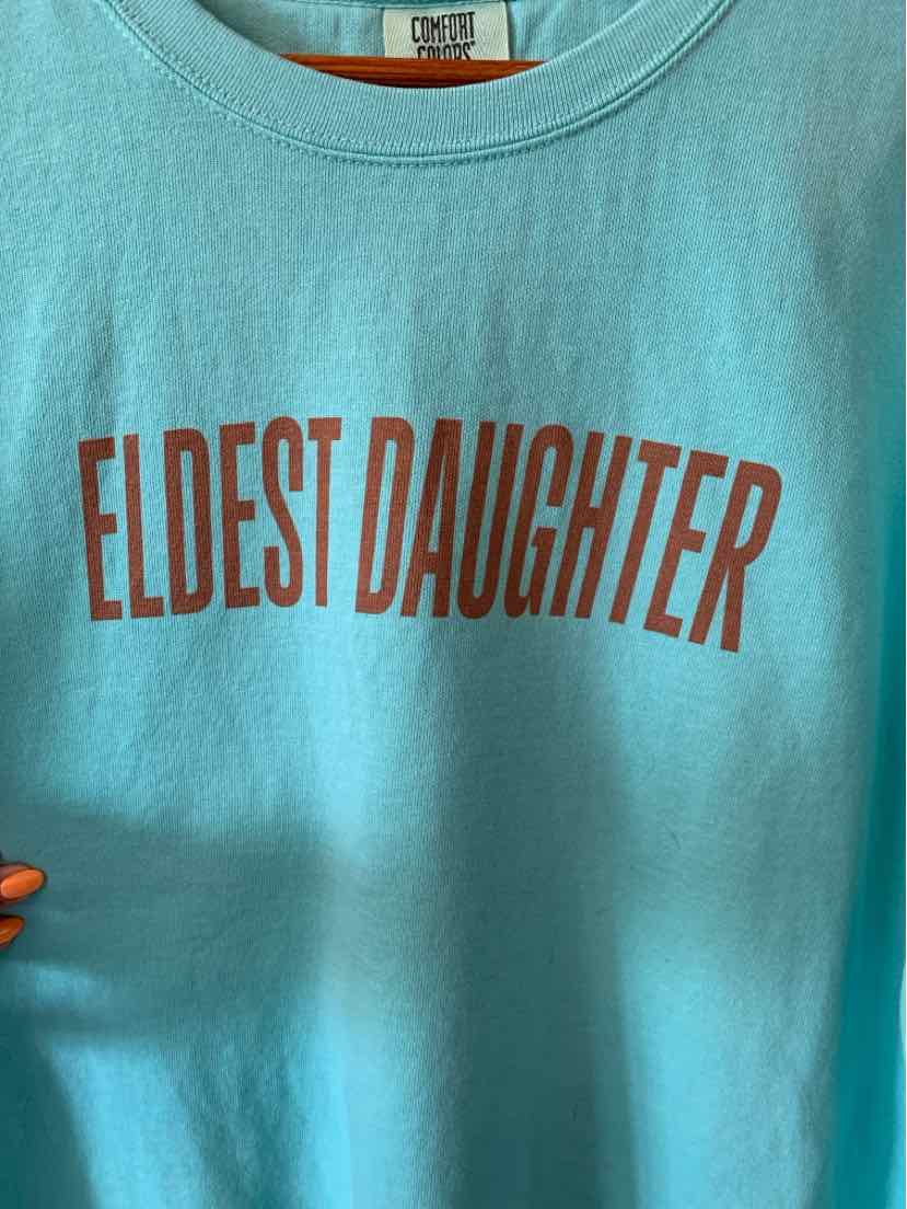 Teal short-sleeve cotton t-shirt with "ELDEST DAUGHTER" printed in bold red letters across the chest.