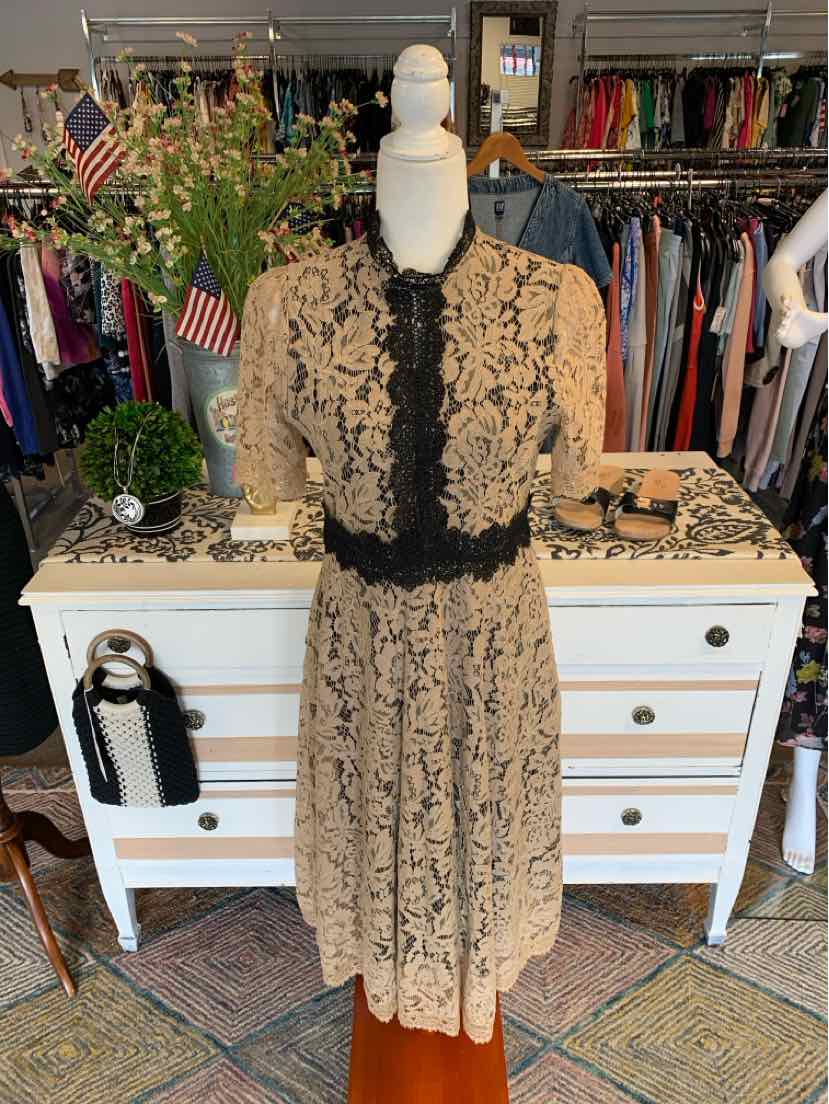 Nude lace midi dress with black floral overlay, short sleeves, black sash belt, and V-neckline.