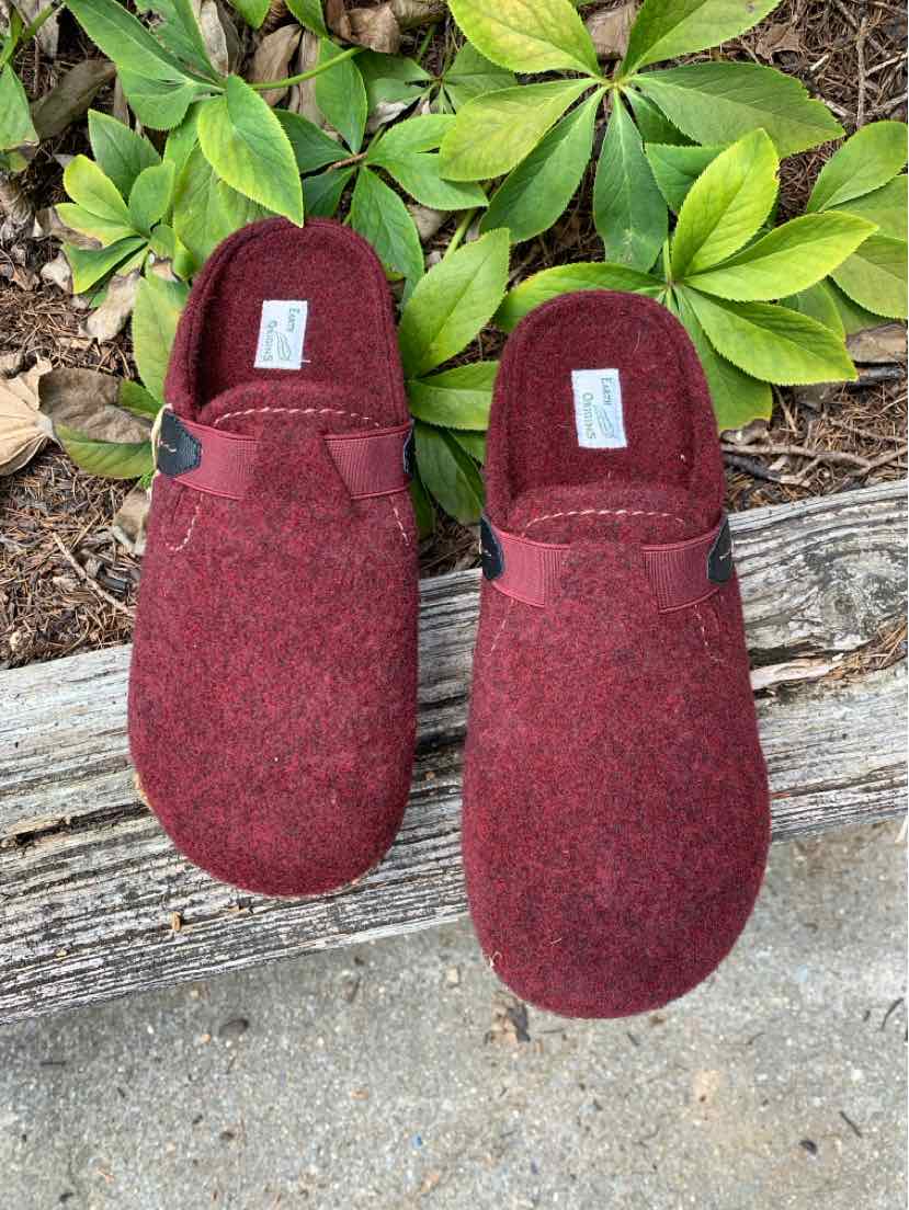 Burgundy slip-on clogs with soft fabric upper and cushioned insoles placed outdoors on wooden and concrete surfaces with.