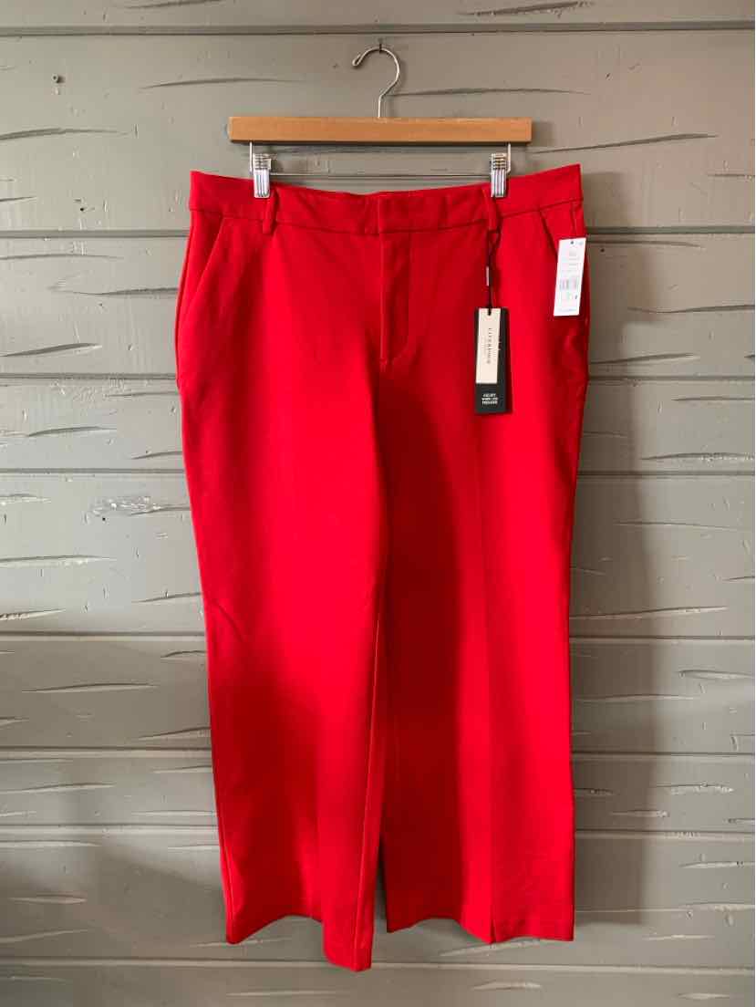 Bright red straight-leg pants with belt loops and tag hanging on wooden hanger against gray wall.