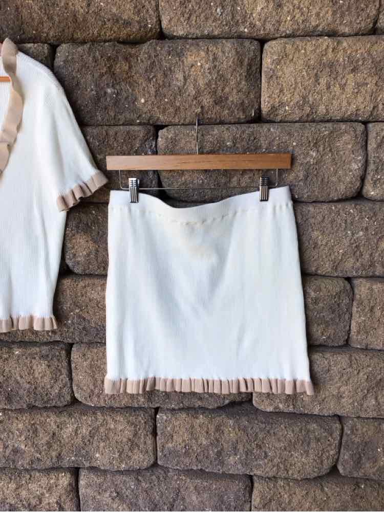 White mini skirt with beige ruffle trim on hem, hanging against stone wall background.