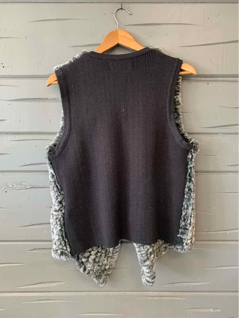 Black sleeveless knit top with gray faux fur trim along sides and hem hanging on wooden hanger against gray wall.