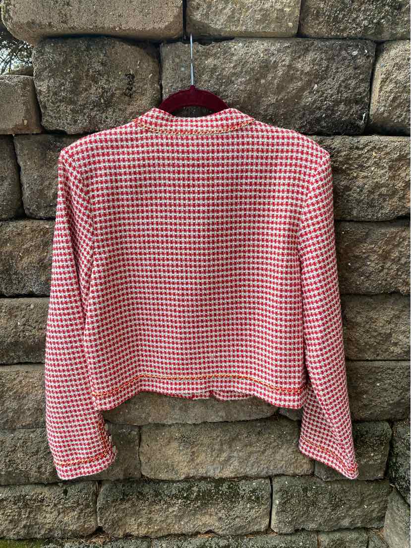 Red and white tweed blazer with long sleeves and a cropped fit hanging against a stone wall.