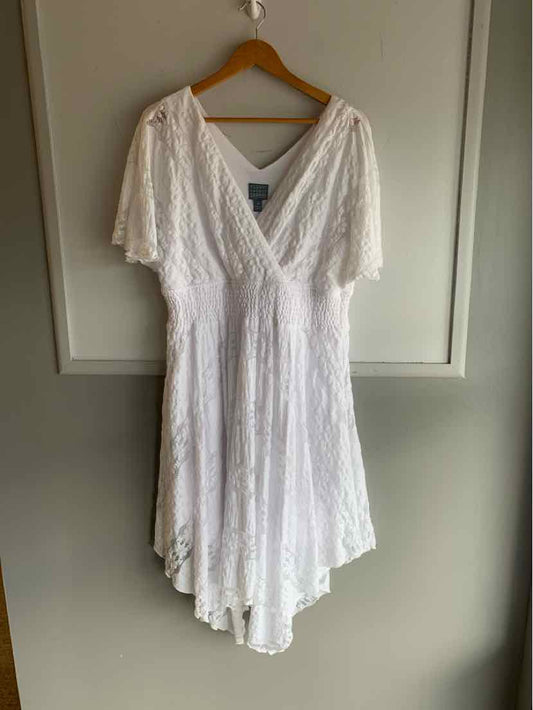 White lace dress with V-neck, flutter sleeves, and asymmetrical hem hanging on wooden hanger.