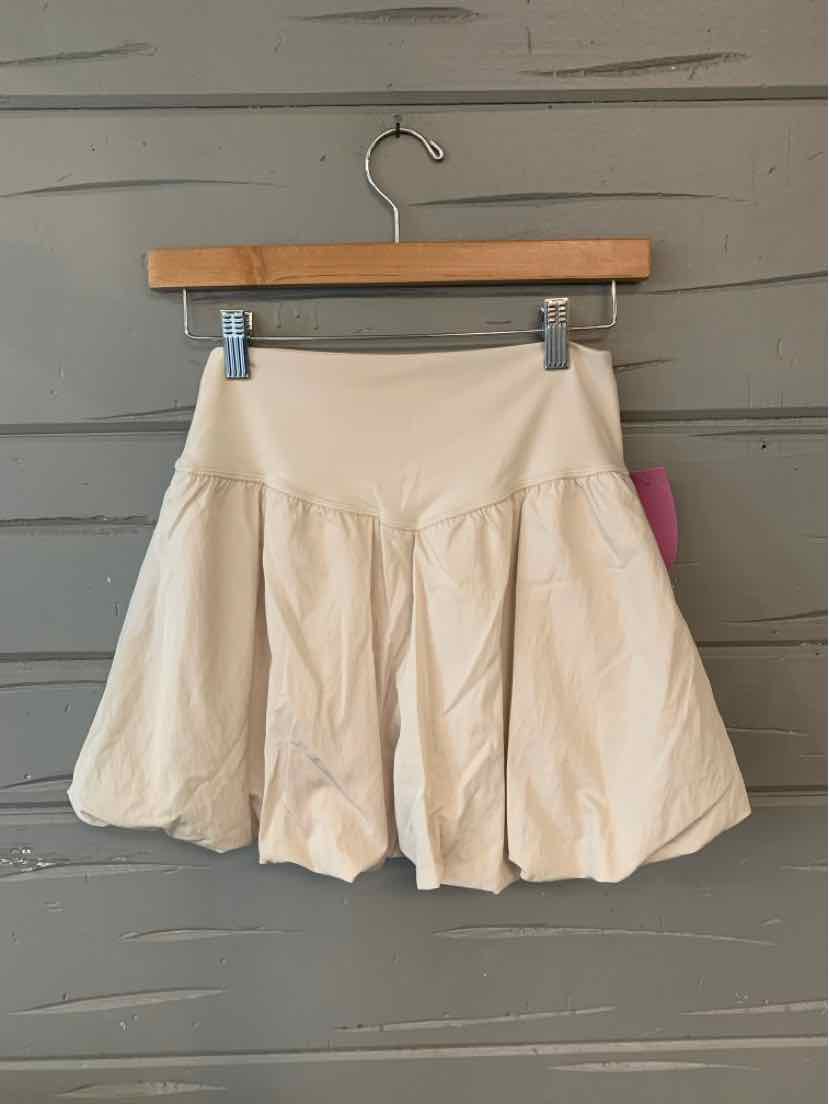 Beige medium skort with wide waistband and flared pleated skirt hanging on wooden hanger.