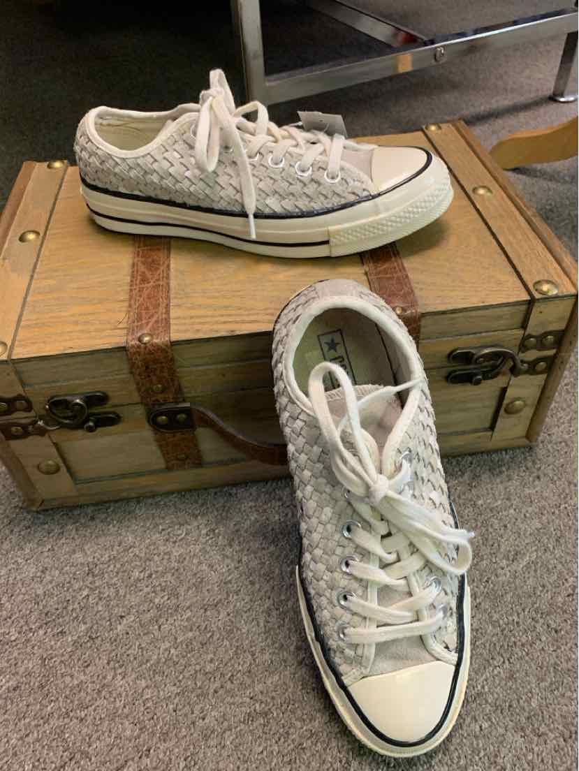 White low-top Converse sneaker with textured pattern, white laces, and black stripe on sole.