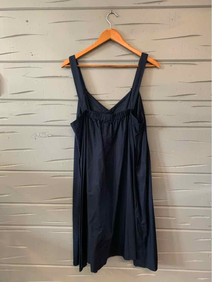 Navy blue sleeveless dress with wide straps and gathered bust hanging on wooden hanger against textured wall.