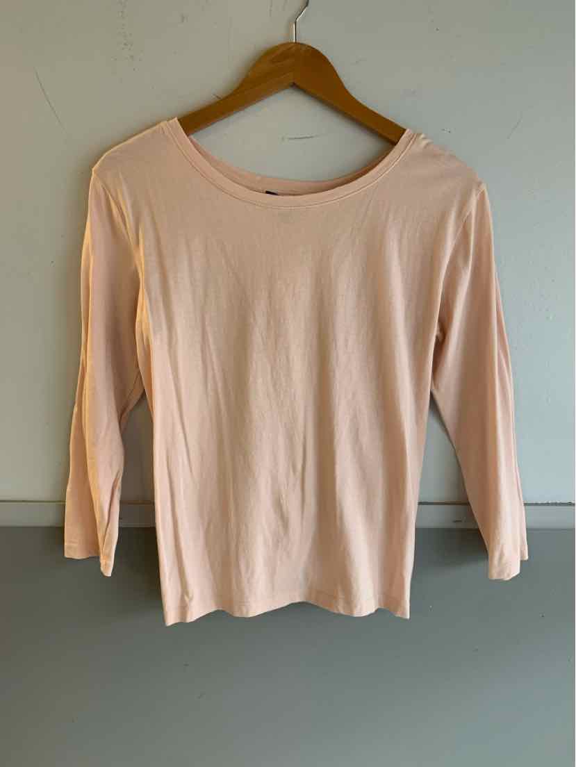 Light pink long-sleeve crew neck top on wooden hanger against plain wall.