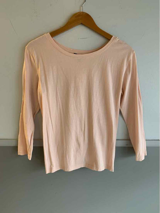 Light pink long-sleeve crew neck top on wooden hanger against plain wall.