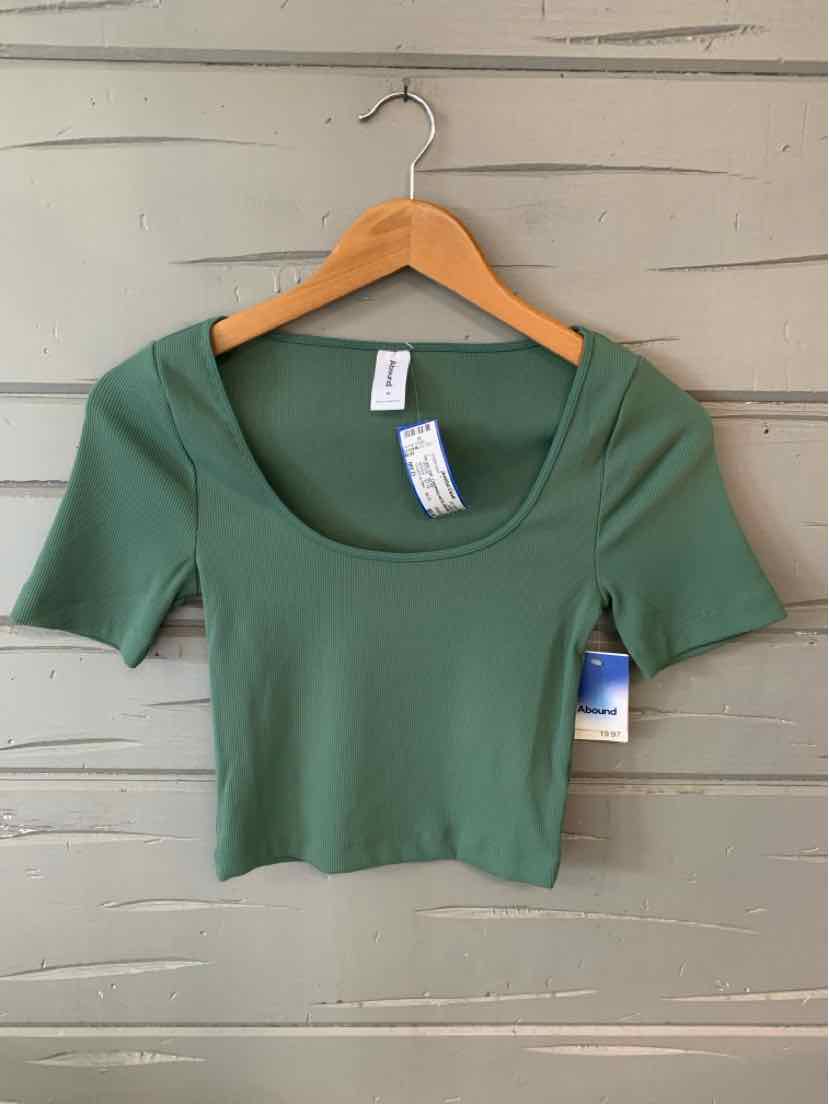 Green short-sleeve crop top with scoop neckline on wooden hanger against beige wall.