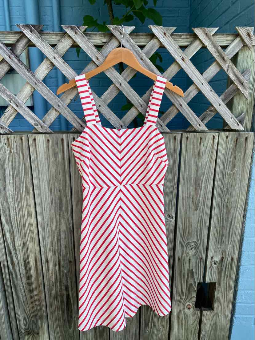White and red striped sleeveless dress with square neckline and fitted bodice hanging on wooden hanger.