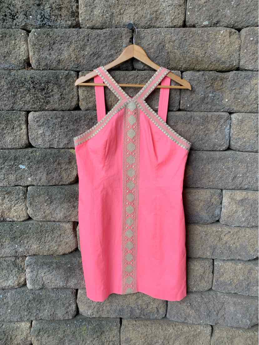 Coral pink sleeveless dress with crisscross straps and embroidered beige trim down front and neckline.
