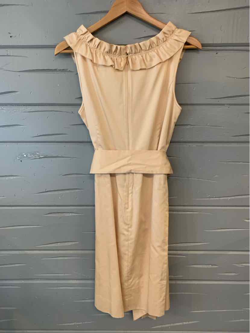 Sleeveless tan dress with ruffled neckline and matching waist belt hanging on wooden hanger.