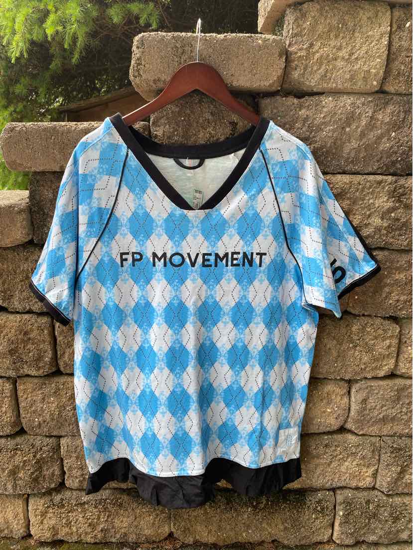 Blue and white argyle pattern short-sleeve top with black V-neck trim and "FP Movement" logo at chest.