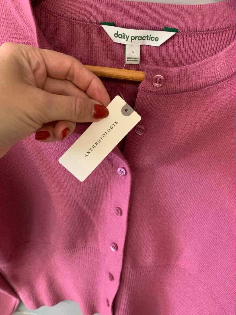 Pink knit cardigan with button front, ribbed trim, and a white clothing tag at the neckline.