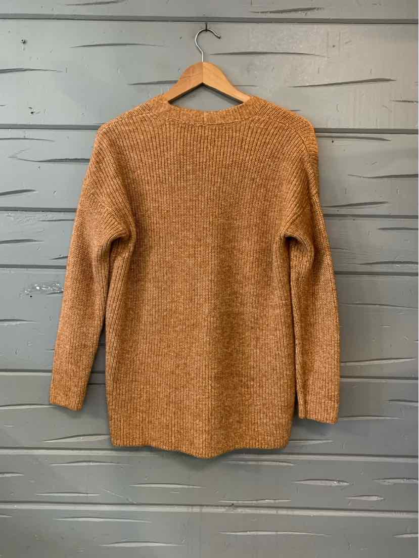 Tan knit long-sleeve tunic sweater with a rounded neckline and relaxed fit, hanging on a wooden hanger.