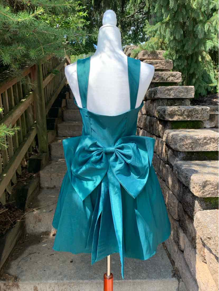 Teal satin sleeveless dress with a deep V-back and large decorative bow at the waist.