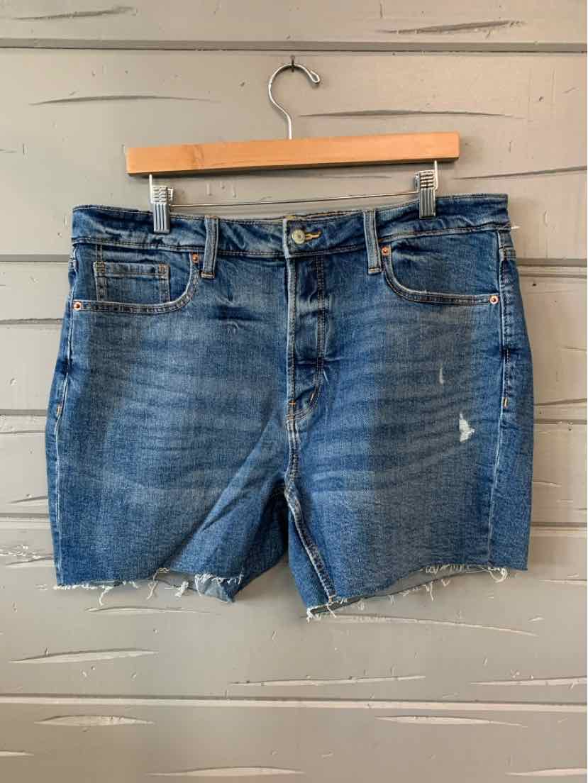 Blue denim Old Navy shorts size 16 with frayed hems and distressed details hanging on wooden hanger against gray wooden.