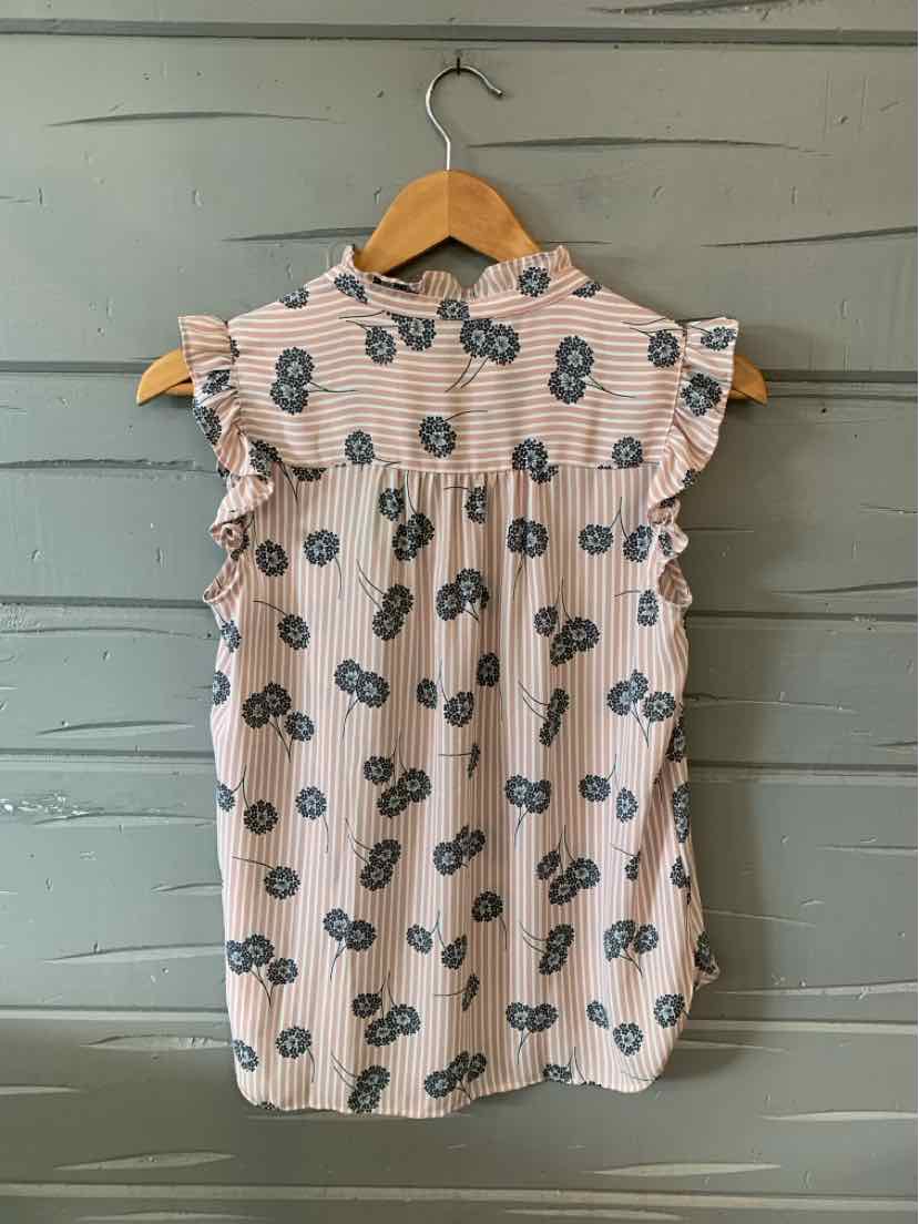 Sleeveless pink blouse with black floral print and ruffled shoulders on wooden hanger.