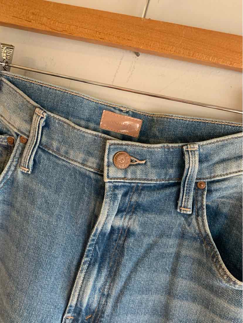 Light blue denim jeans with a front button closure and belt loops hanging on a wooden hanger.