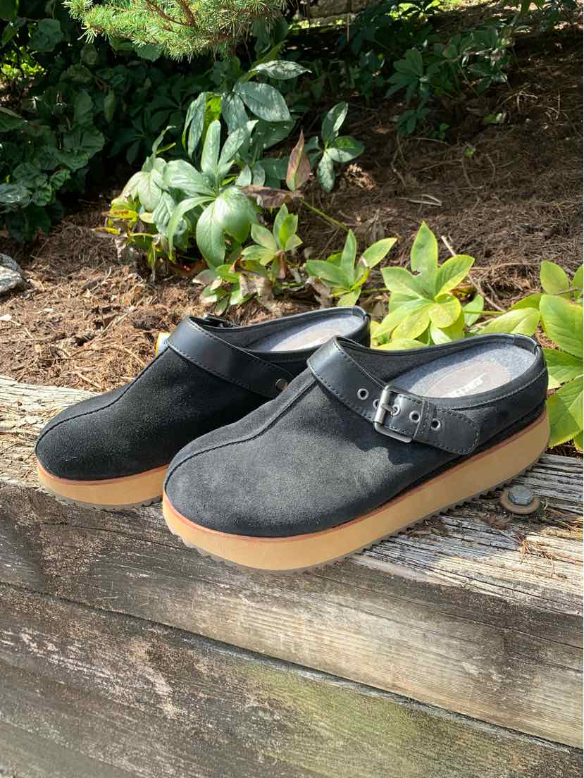 Black slip-on clogs with suede upper, adjustable buckle strap, and light brown rubber sole.