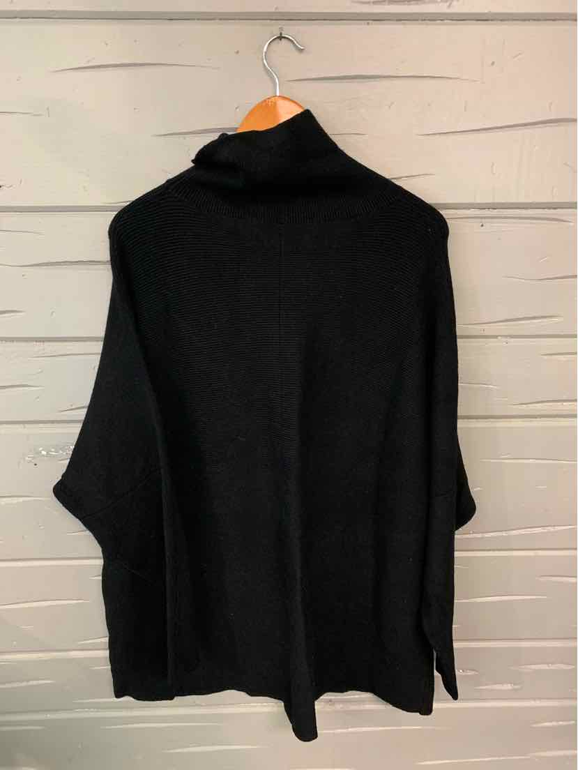 Black oversized turtleneck sweater with loose long sleeves hanging on wooden hanger.