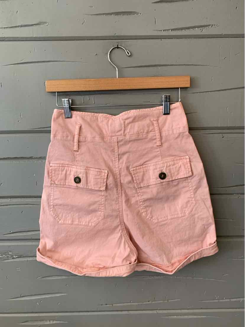 Light pink high-waist shorts with front flap pockets and button closures on wooden hanger.