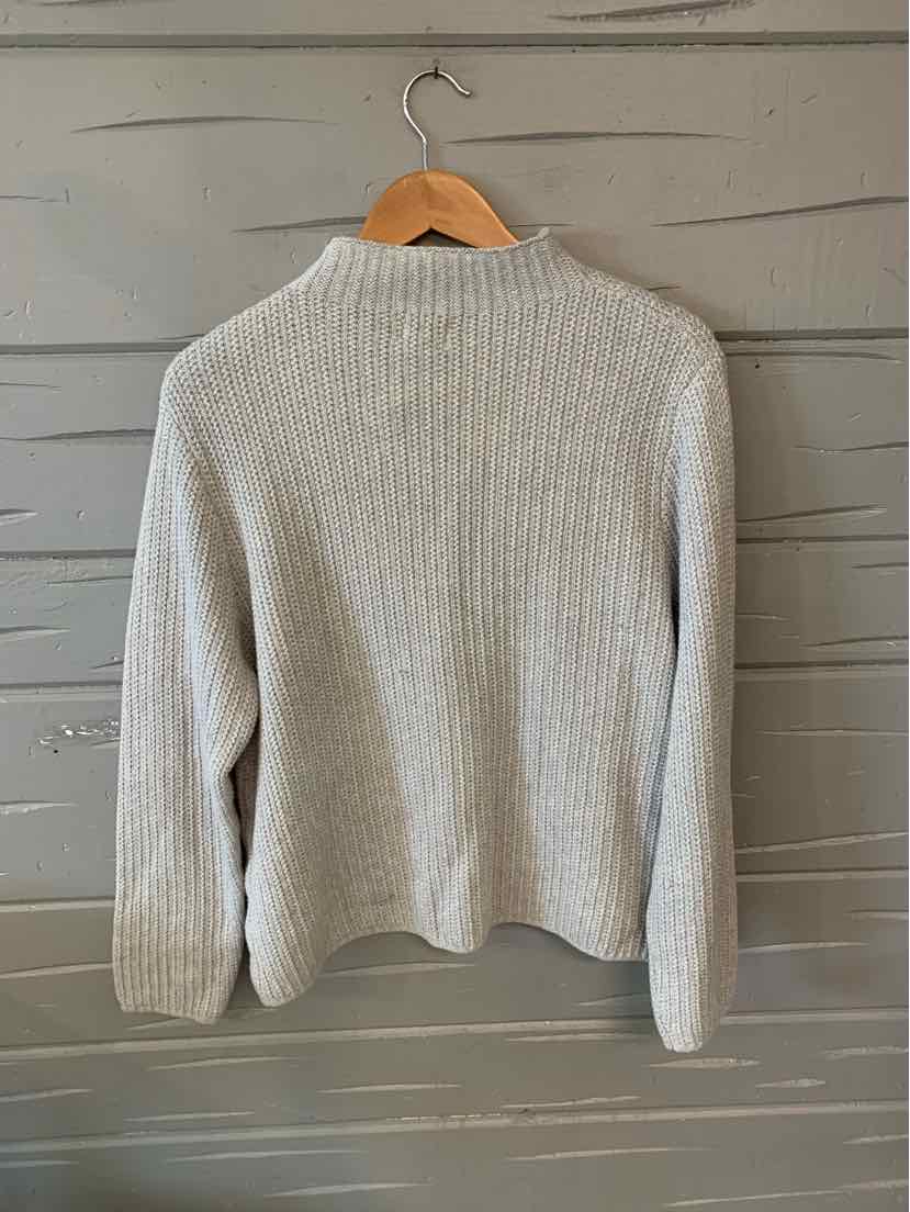 Light gray ribbed knit sweater with long sleeves hanging on wooden hanger against gray wall.